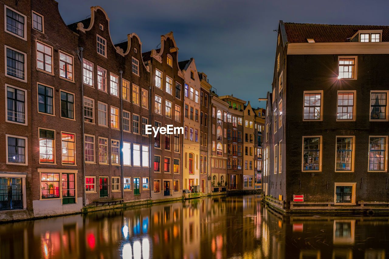 REFLECTION OF BUILDINGS ON WATER IN CITY AT NIGHT