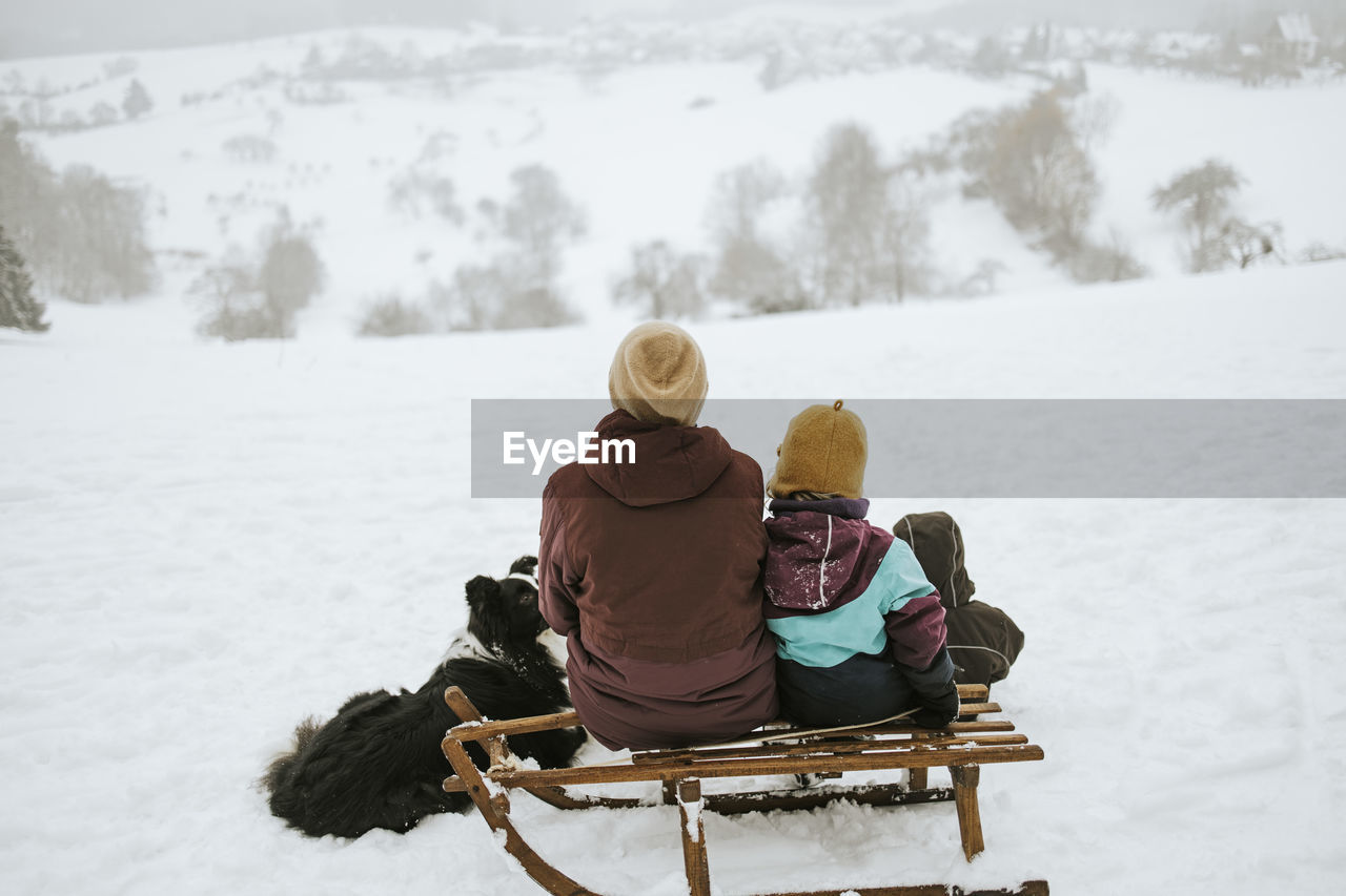 Mother and children with border collie sitting on snow covered field against mountain