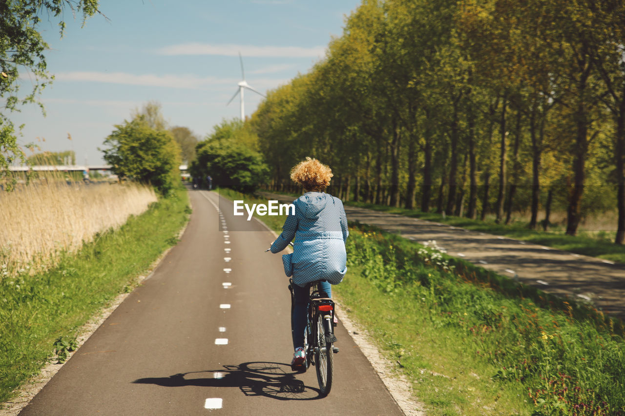 Rear view of woman with curly hair riding bicycle during sunny day