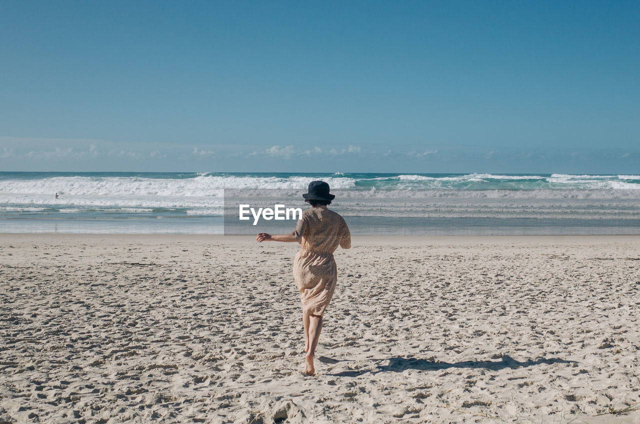 Rear view of woman running at beach against sky