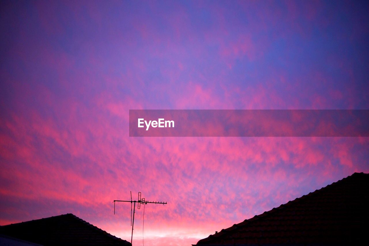 Low angle view of silhouette communications tower against sky at sunset