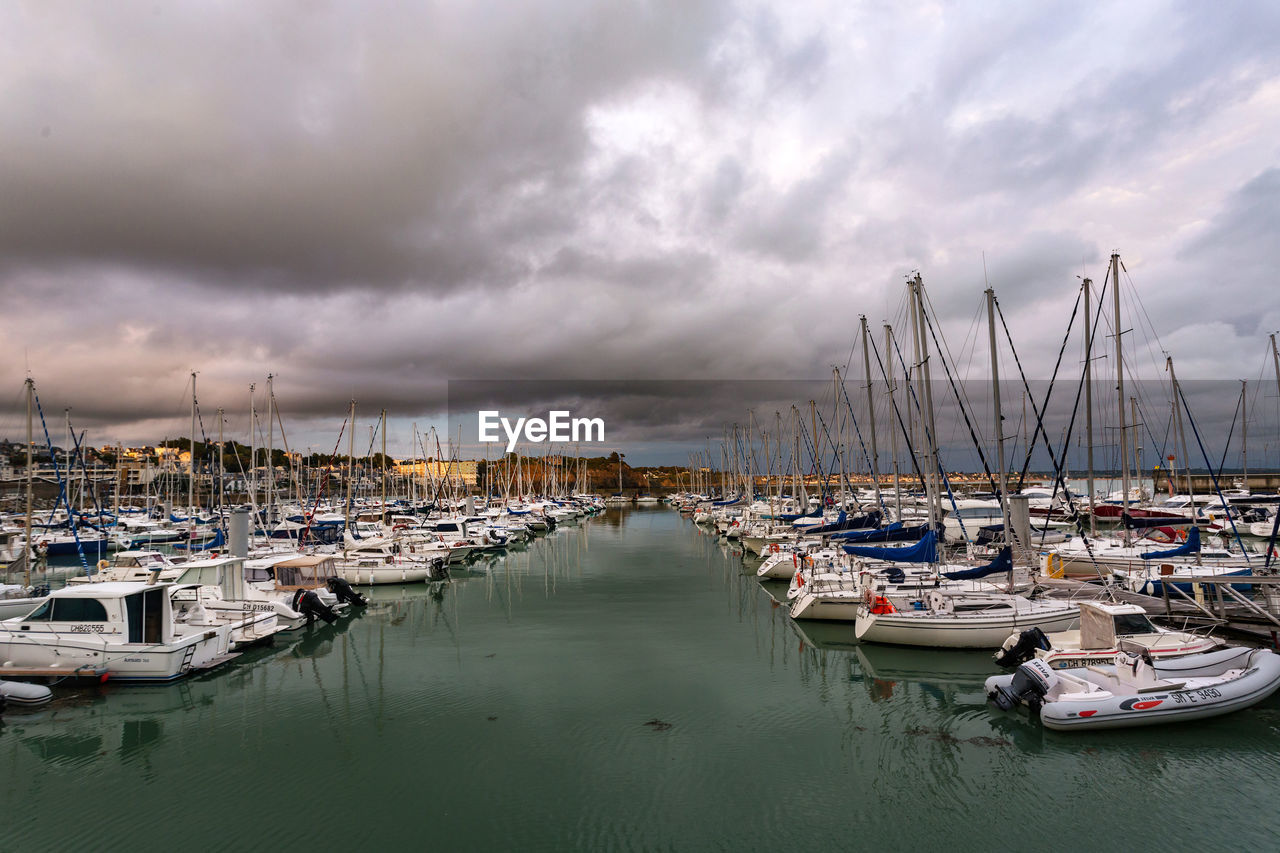 SAILBOATS MOORED IN HARBOR AGAINST SKY