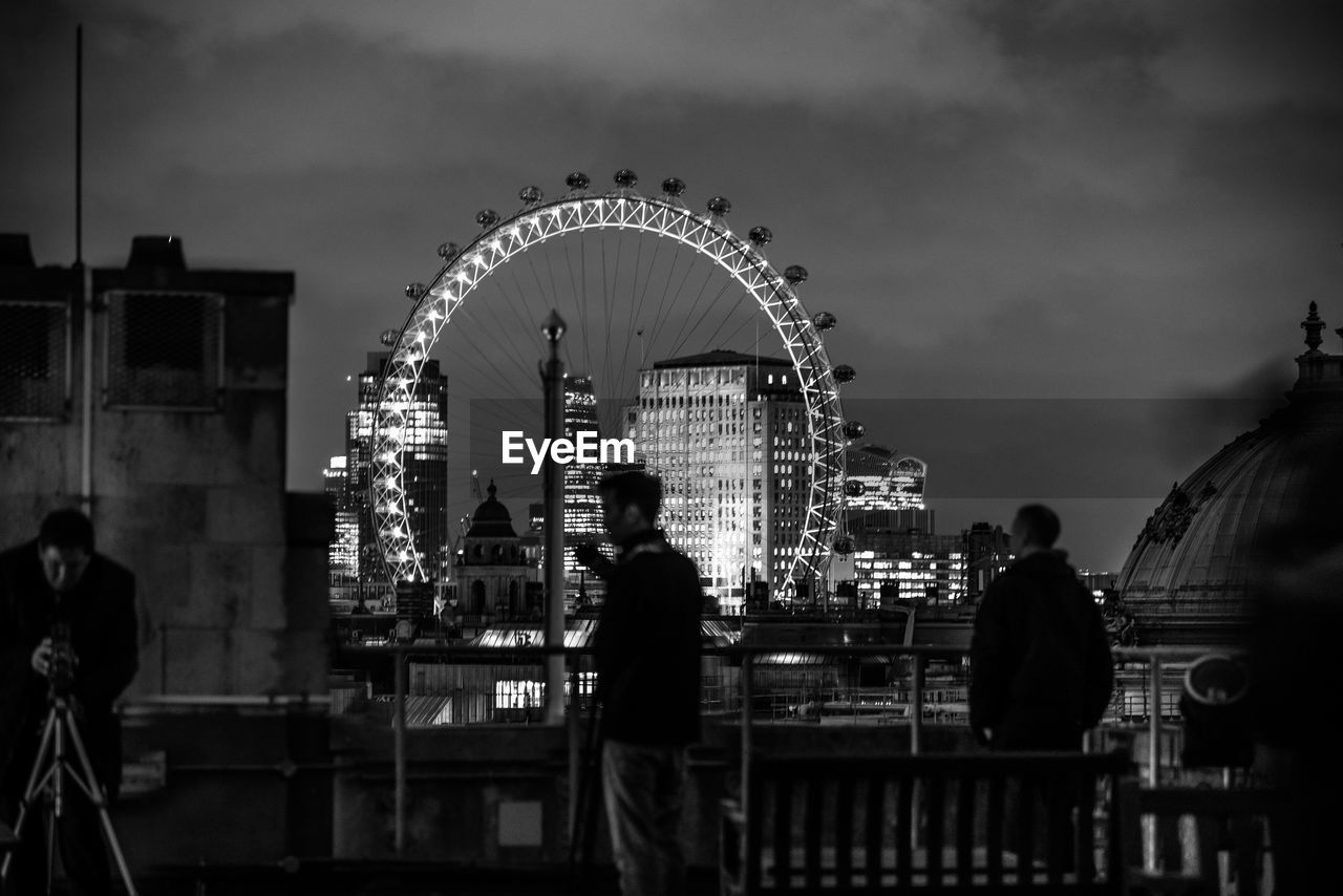 Men standing on bridge against millennium wheel at night