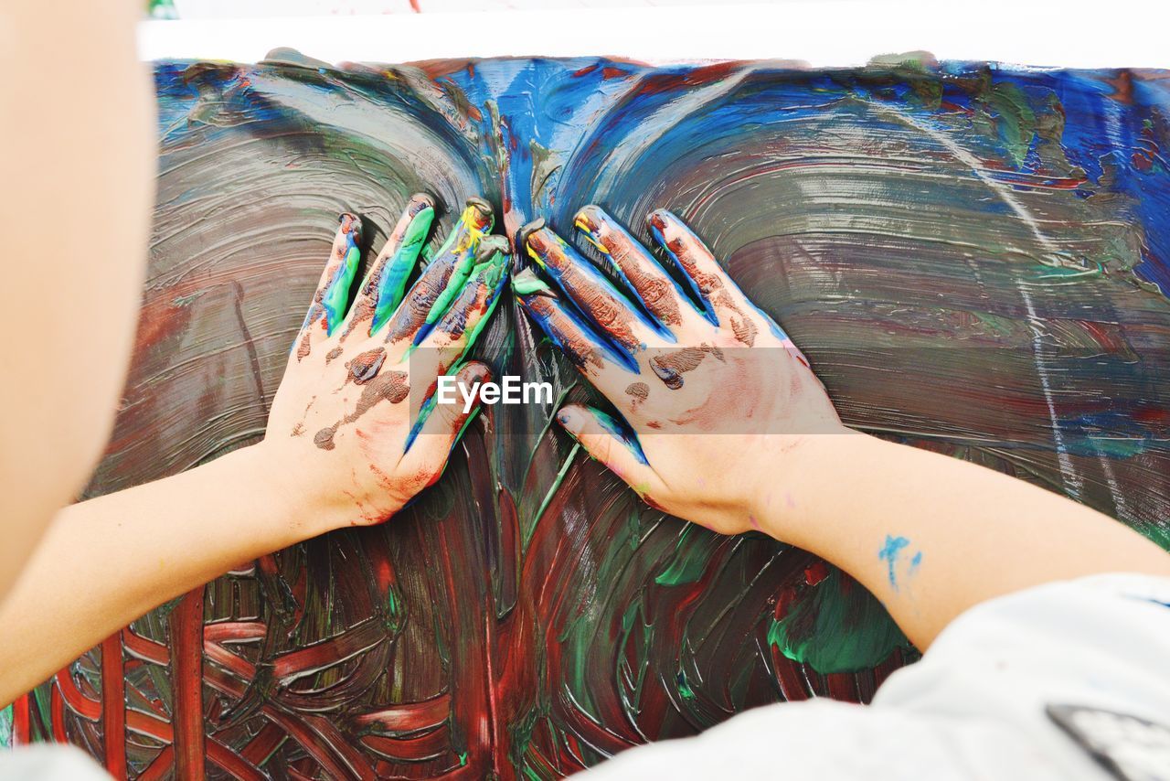 Cropped image of boy painting on canvas with hands