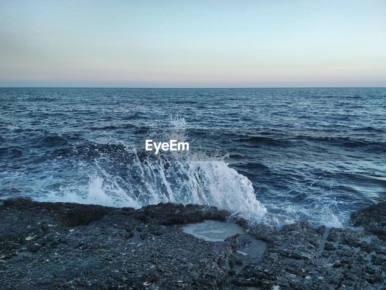 Waves splashing on rock at sea against sky