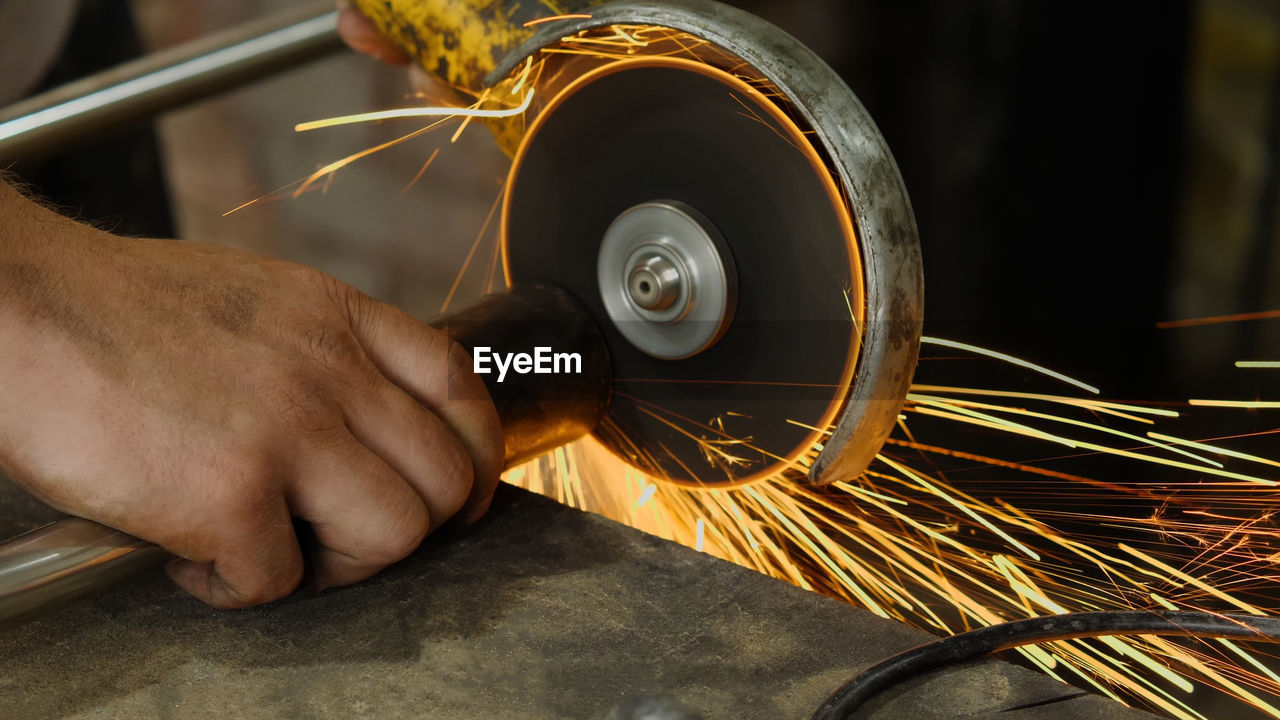 hand, occupation, wheel, one person, working, close-up, adult, skill, industry, indoors, manual worker, yellow, men, workshop, work tool, metal, business finance and industry, equipment, metal industry, business, craft, metalworking, technology, sparks, holding, motion, accuracy, expertise, iron, heat, factory