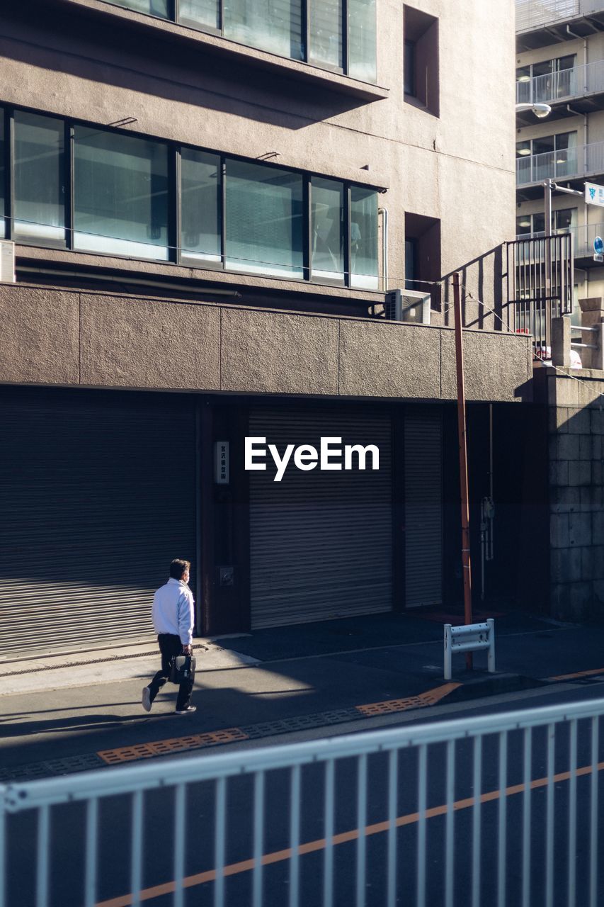 FULL LENGTH OF MAN WALKING ON STREET AGAINST BUILDING