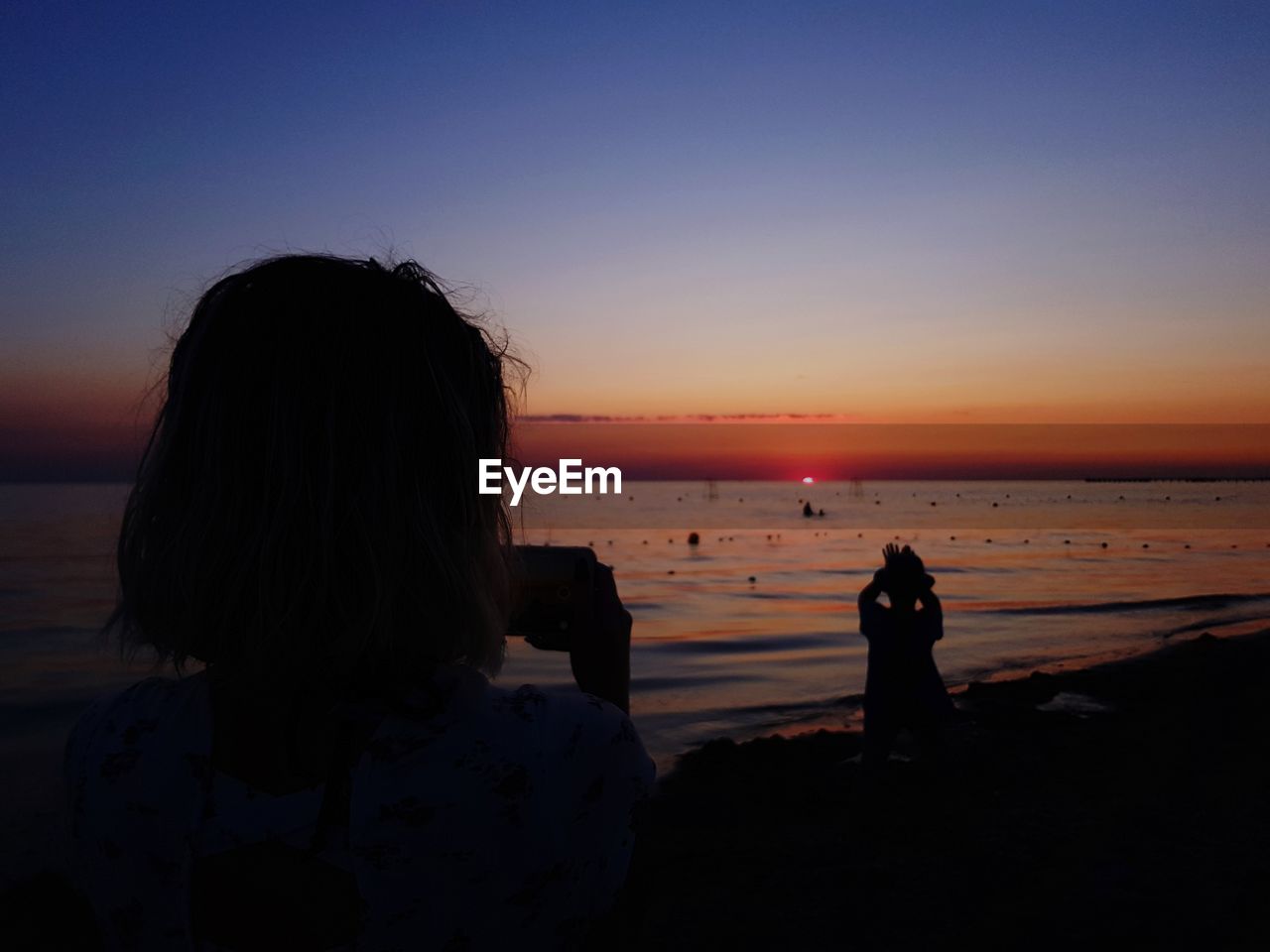 REAR VIEW OF SILHOUETTE PEOPLE LOOKING AT SEA DURING SUNSET