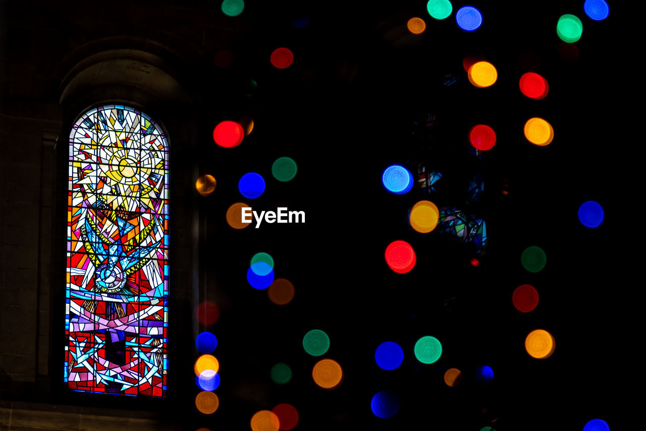 Detail of a colorful stained glass window from inside of church, seen across a beautiful bokeh