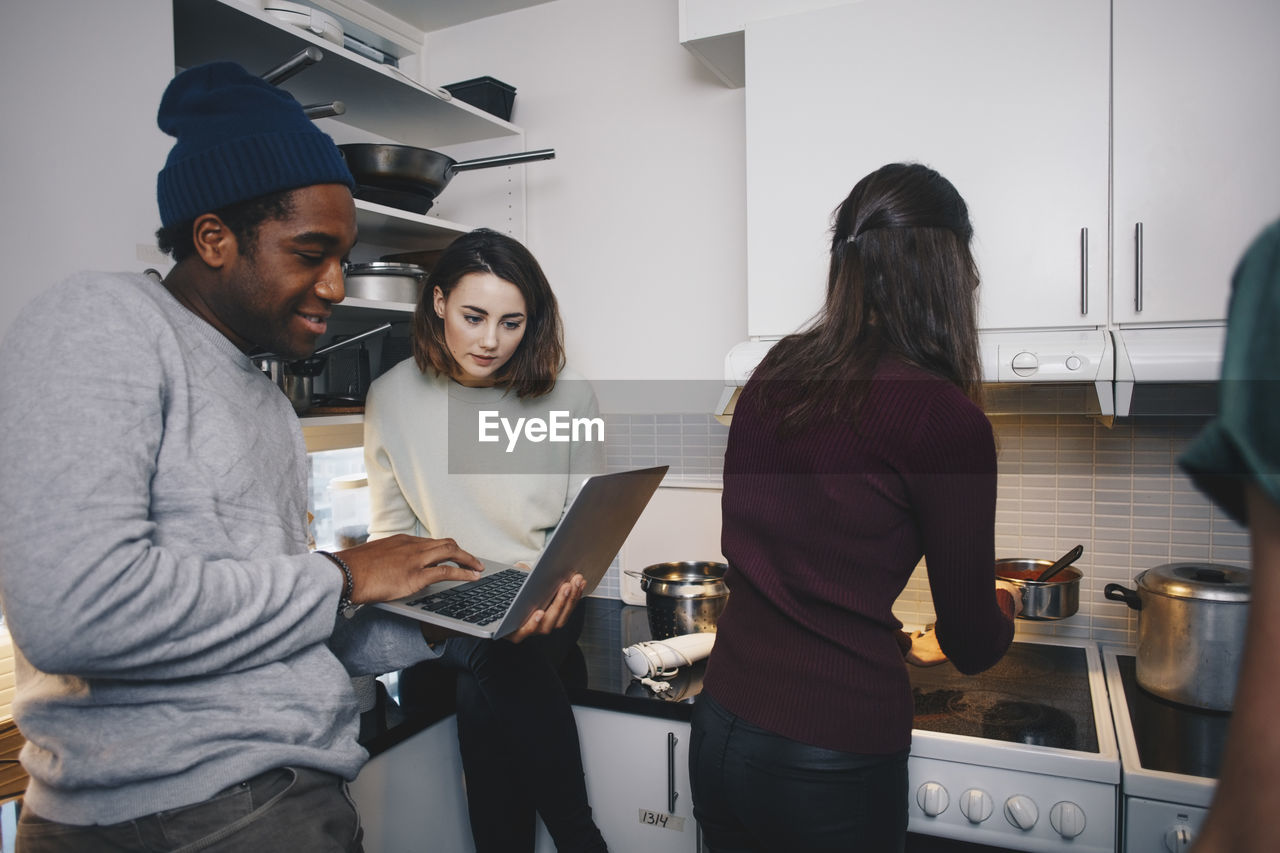 Man showing laptop to female friend in kitchen