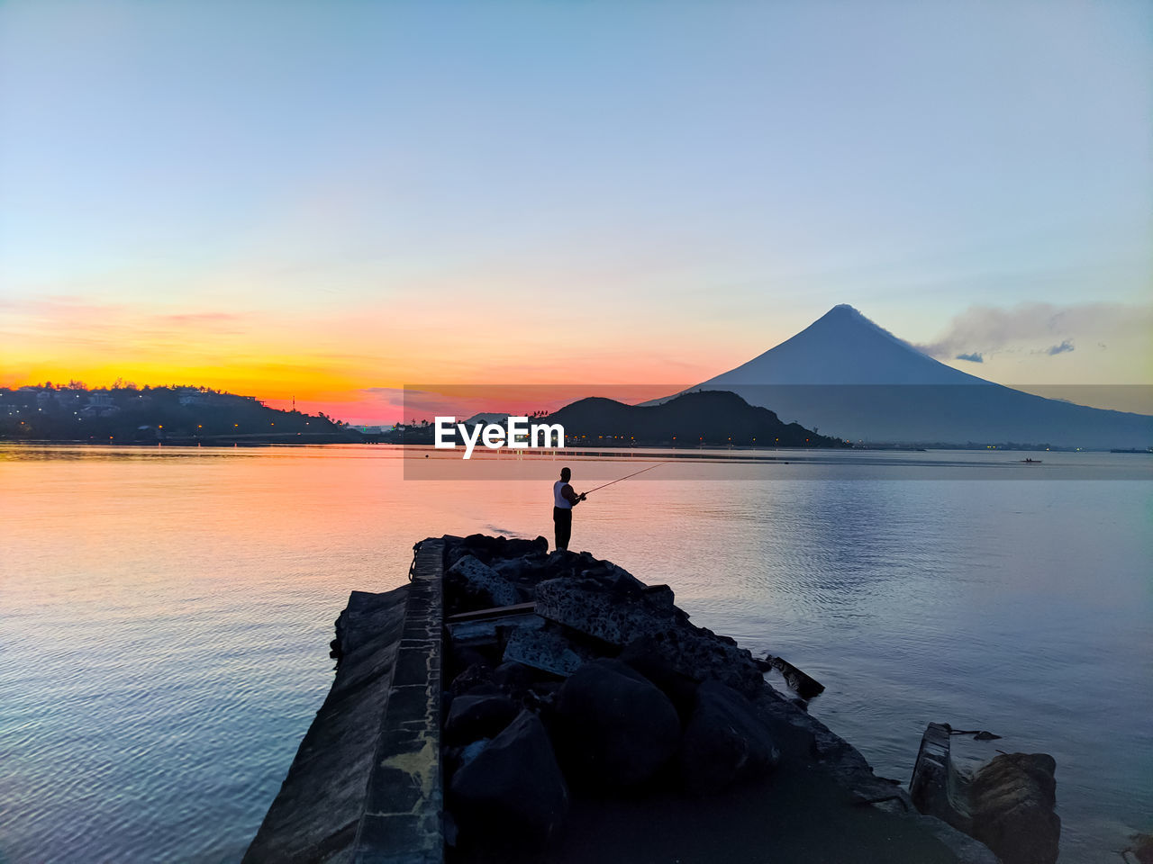 Man standing on rock against sky during sunset