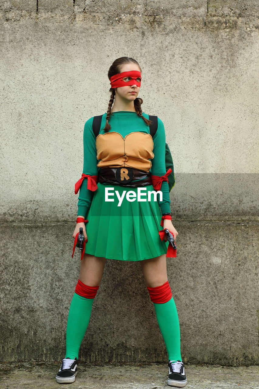 Young woman looking away wearing costume standing against wall