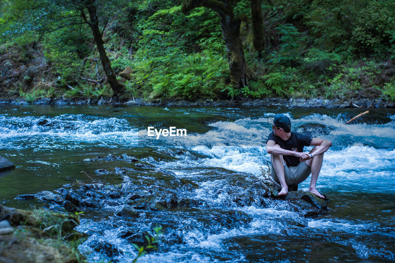 Young man sitting by river in forest