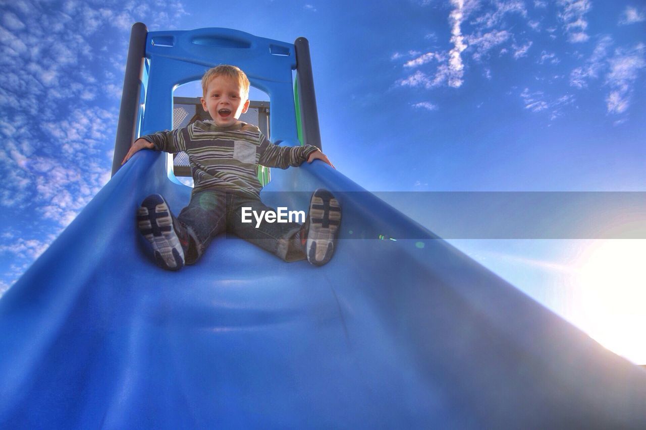 Portrait of a cute little boy on slide against blue sky