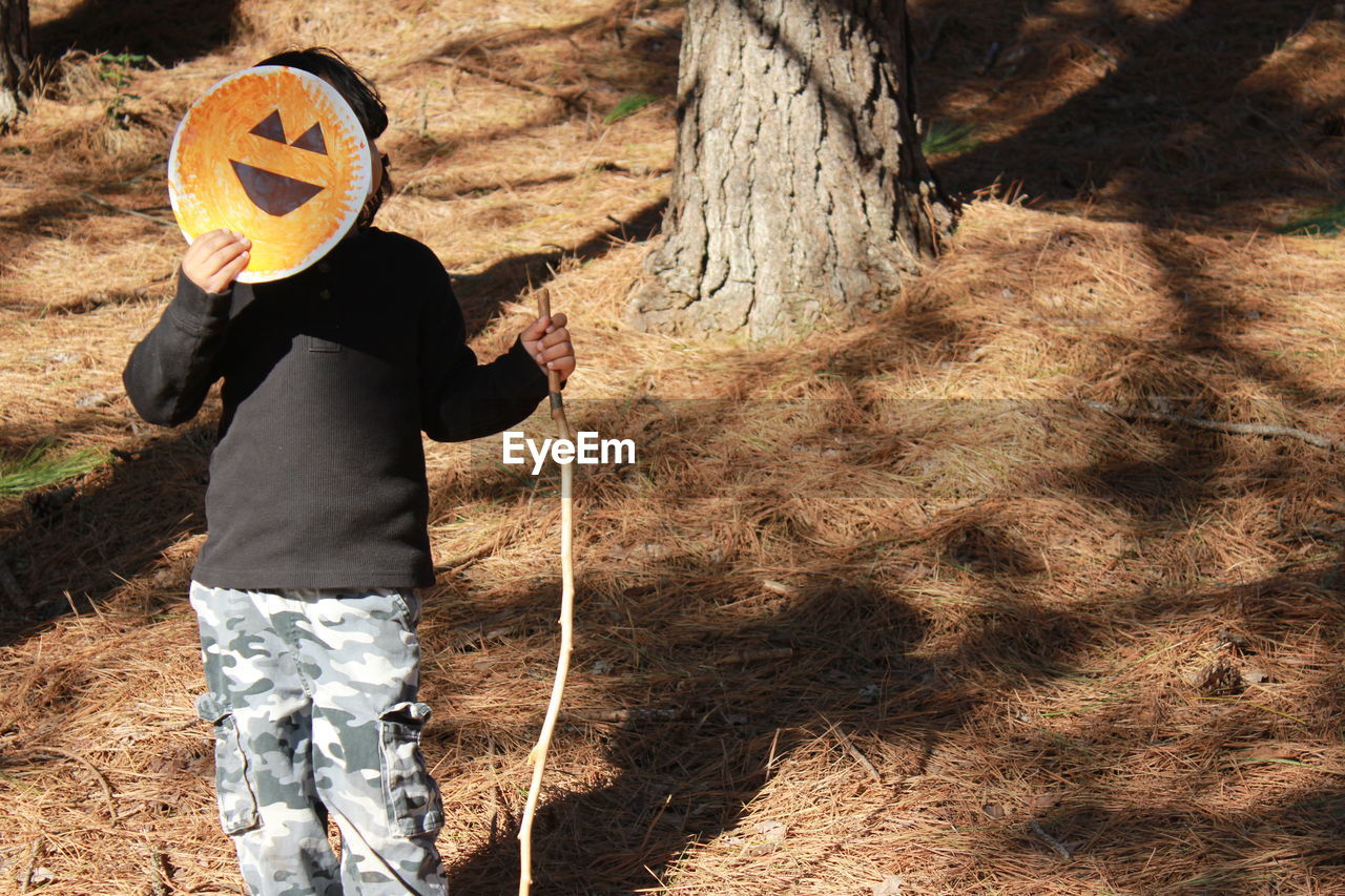 Boy holding art on paper over face while standing in forest