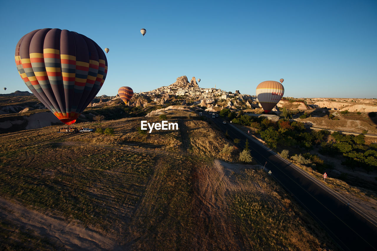 hot air balloon, balloon, air vehicle, vehicle, transportation, aircraft, hot air ballooning, flying, mid-air, adventure, travel, sky, mode of transportation, nature, landscape, environment, travel destinations, ballooning festival, rock, tourism, journey, multi colored, blue, clear sky, cloud, land, outdoors, basket, scenics - nature, morning, rock formation, mountain, no people, trip, vacation, motion, holiday, day, non-urban scene, beauty in nature, taking off, sunrise