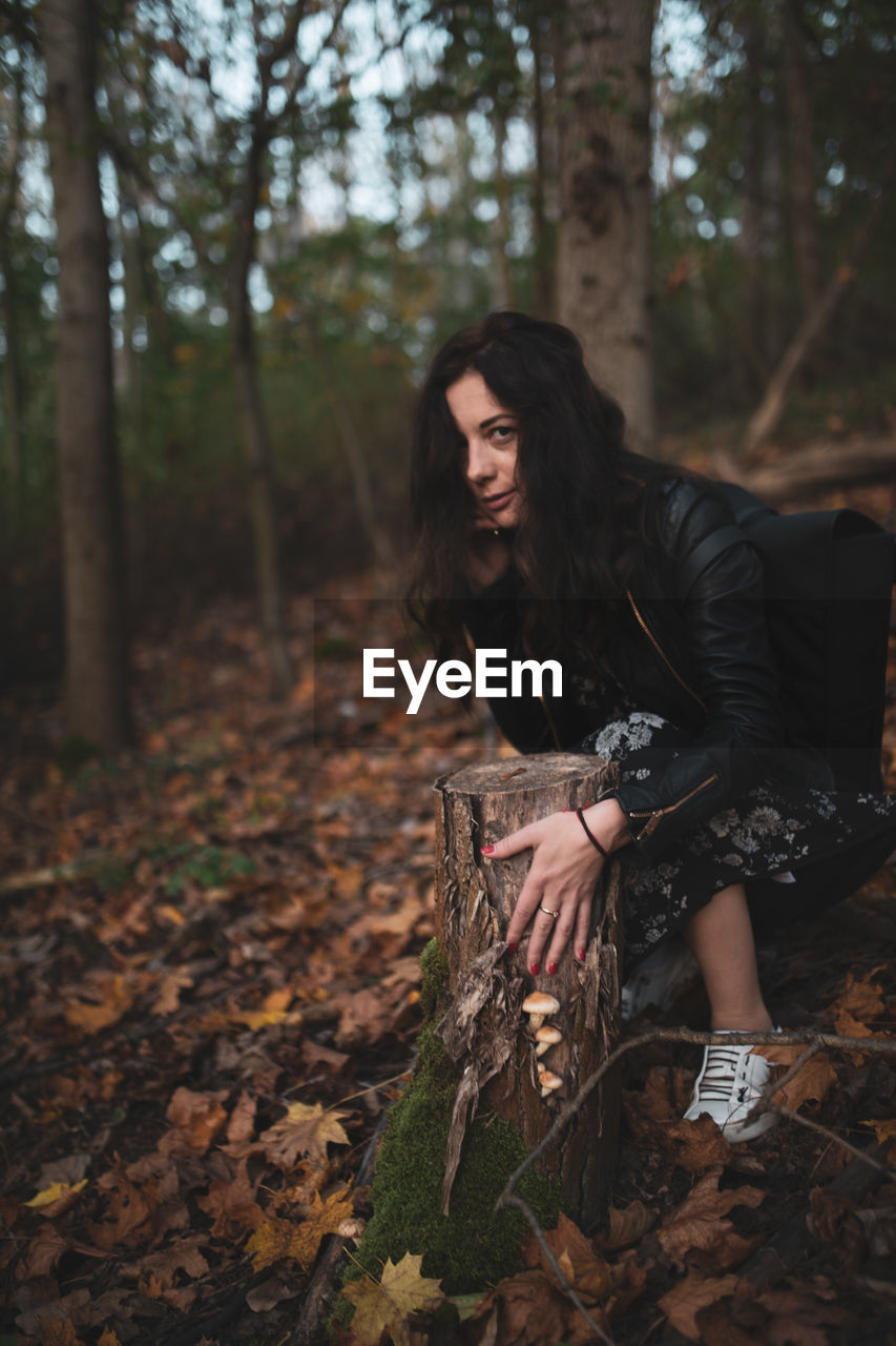 Portrait of woman by tree stump in forest