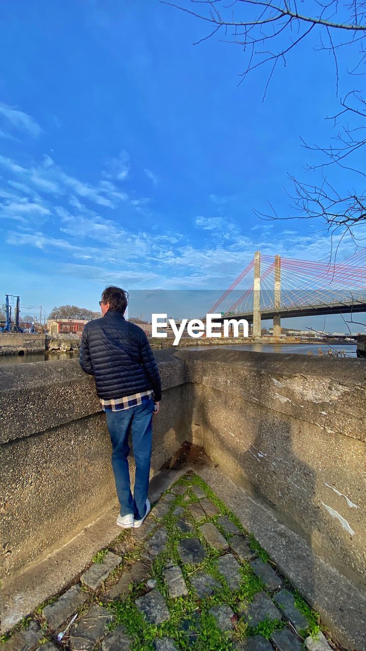 REAR VIEW OF MAN STANDING ON BRIDGE