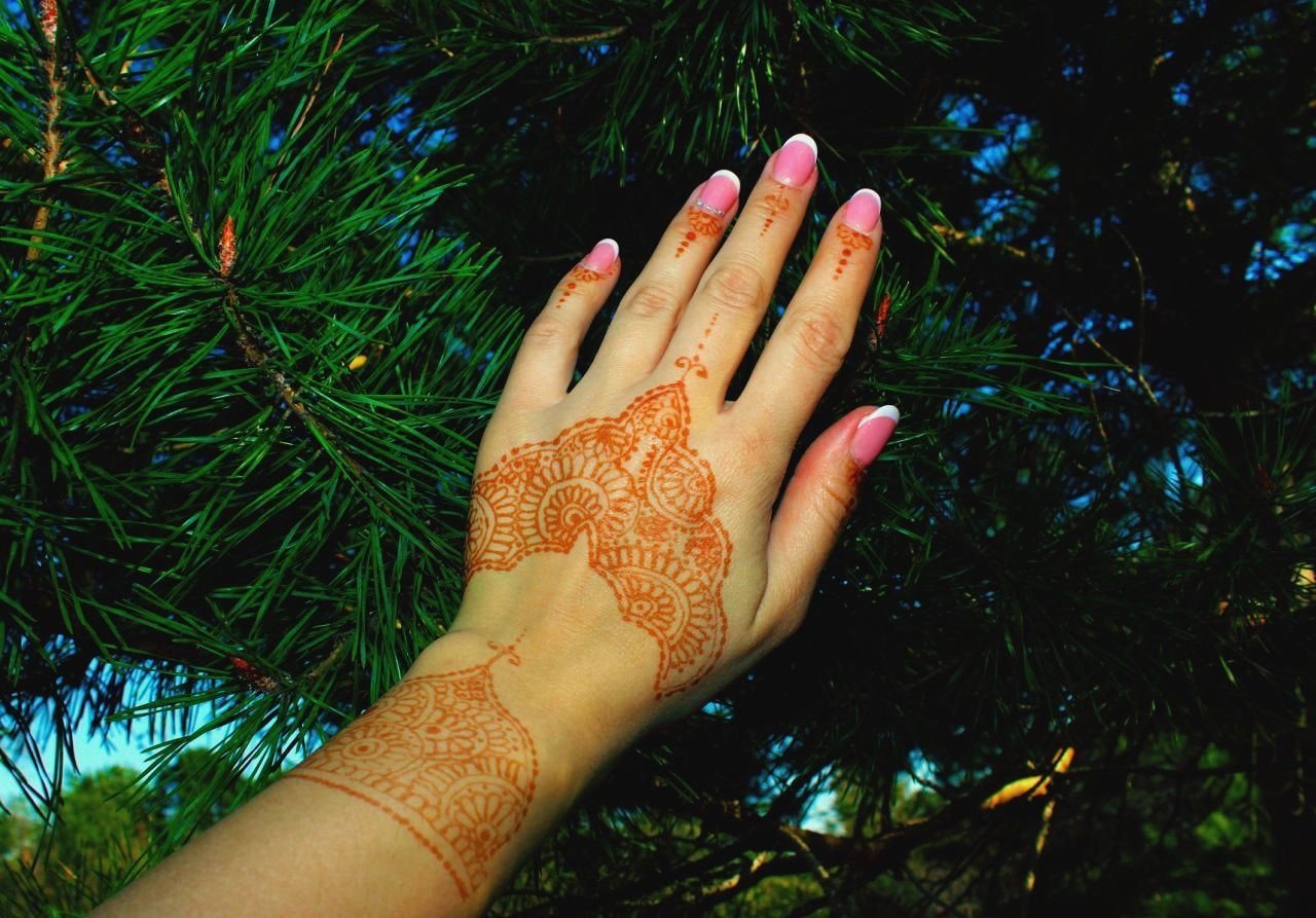 Cropped hand of woman with henna tattoo against pine tree