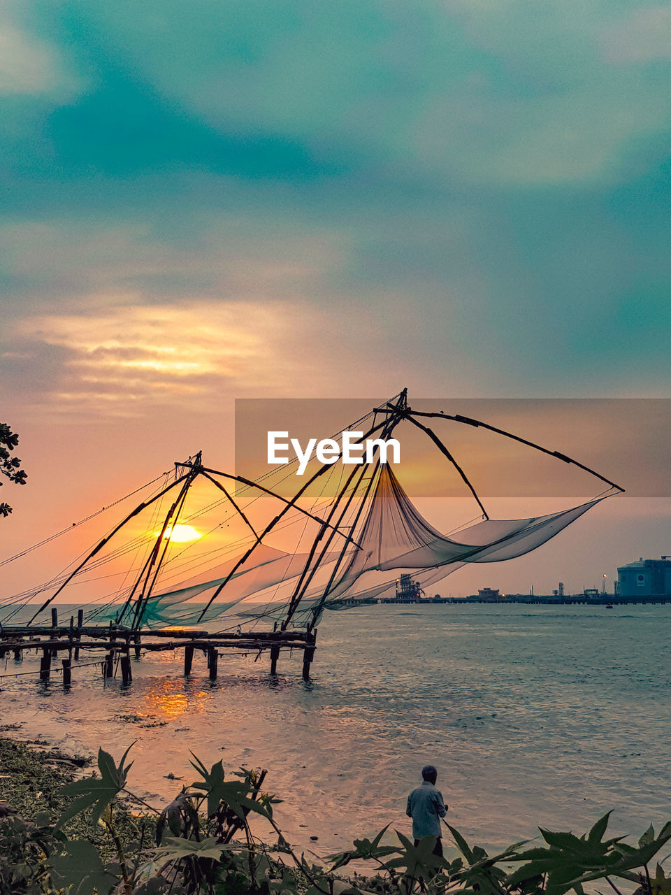 Fishing nets in sea against sky during sunset