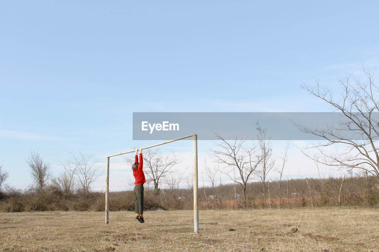 Boy hanging on pole against sky