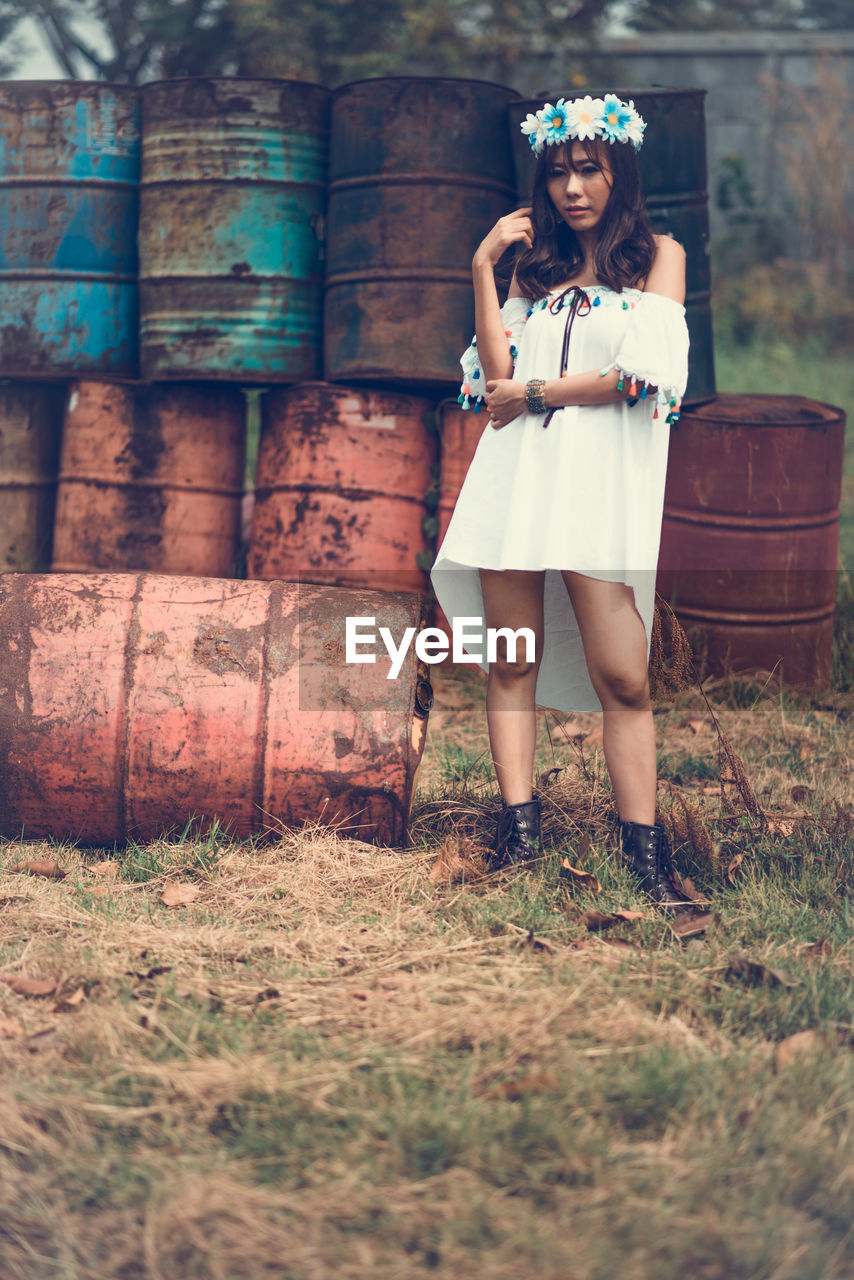 Portrait of woman standing against old containers on field