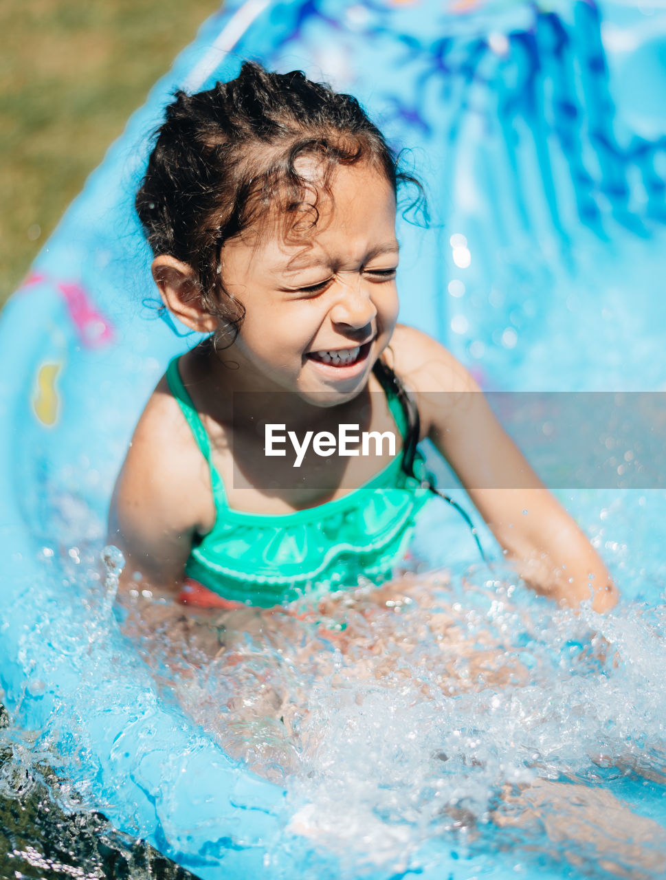 Cute smiling girl sitting in wading pool outdoors