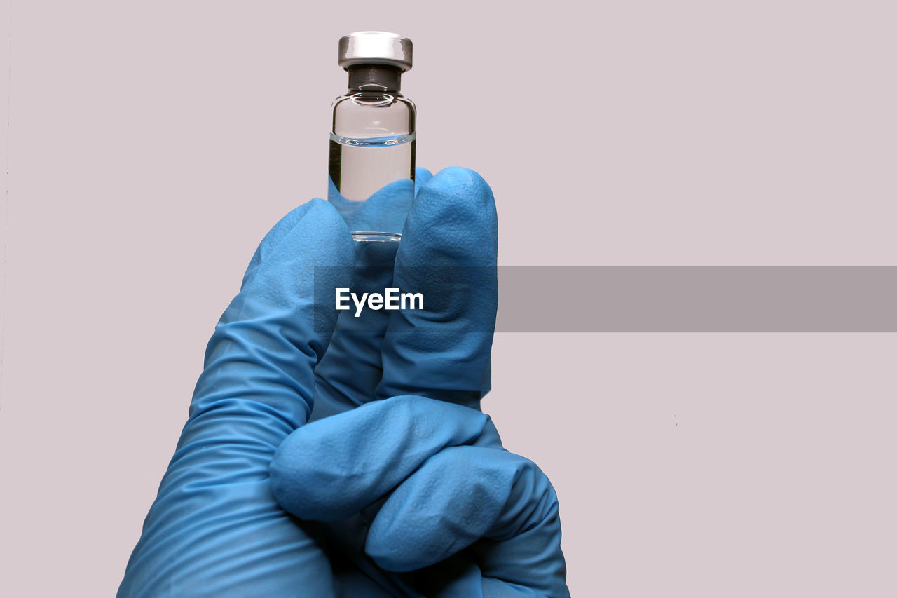 A hand in a blue medical glove close-up holding a vaccine against a light background. 