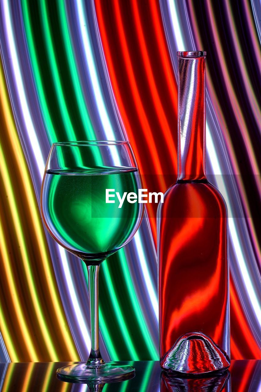 Glass wine and bottle against neon background