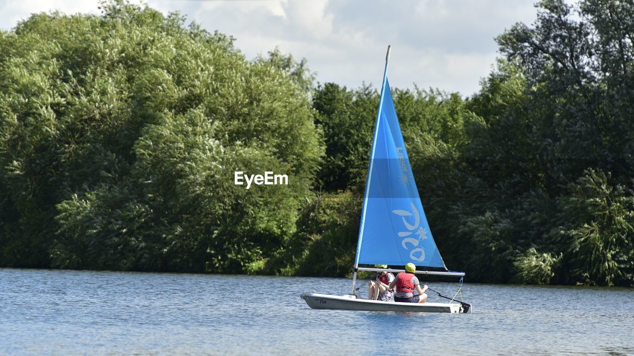 BOAT SAILING IN RIVER AGAINST SKY