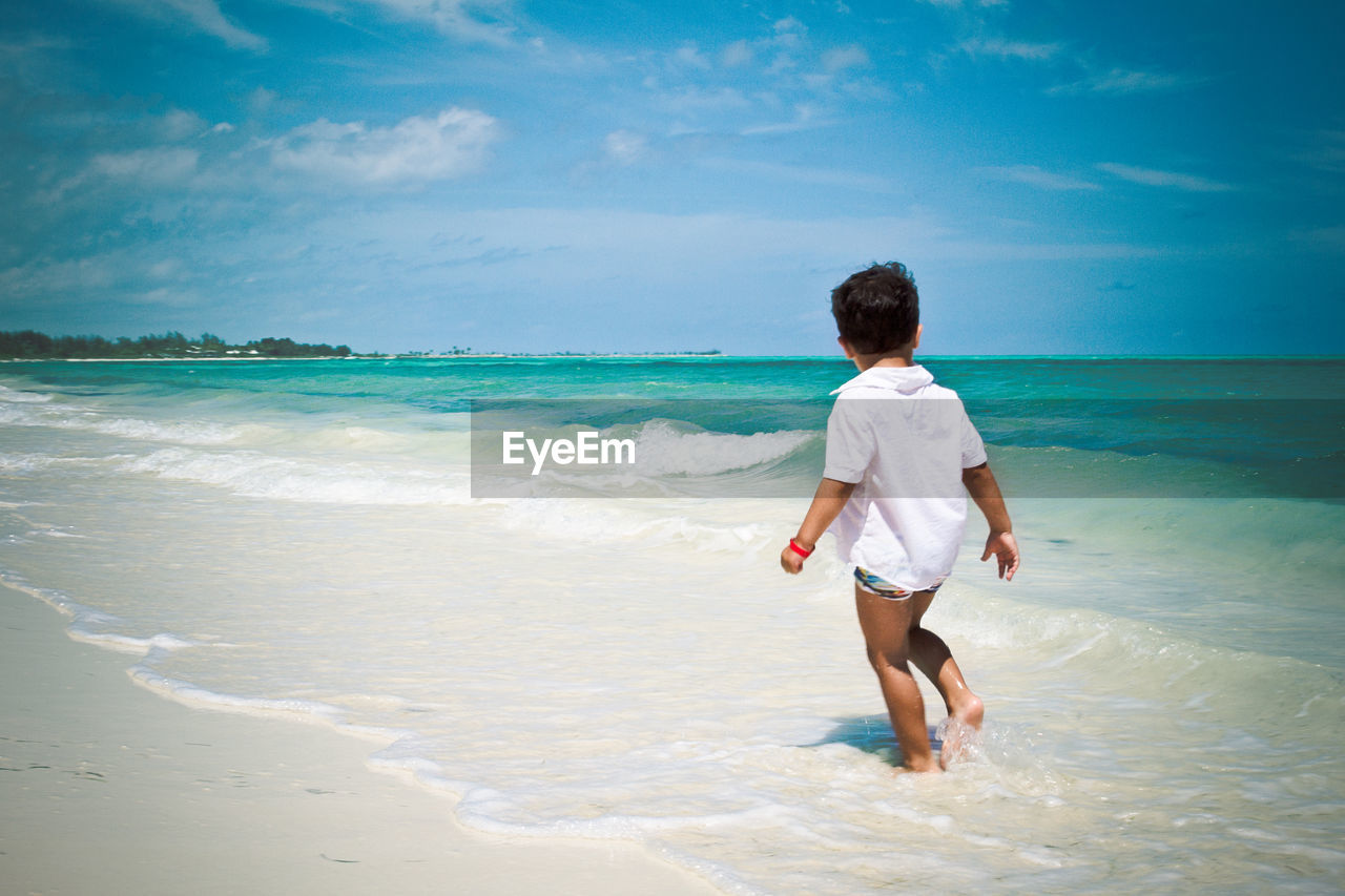 Little boy walking at the beach watching caribbean ocean
