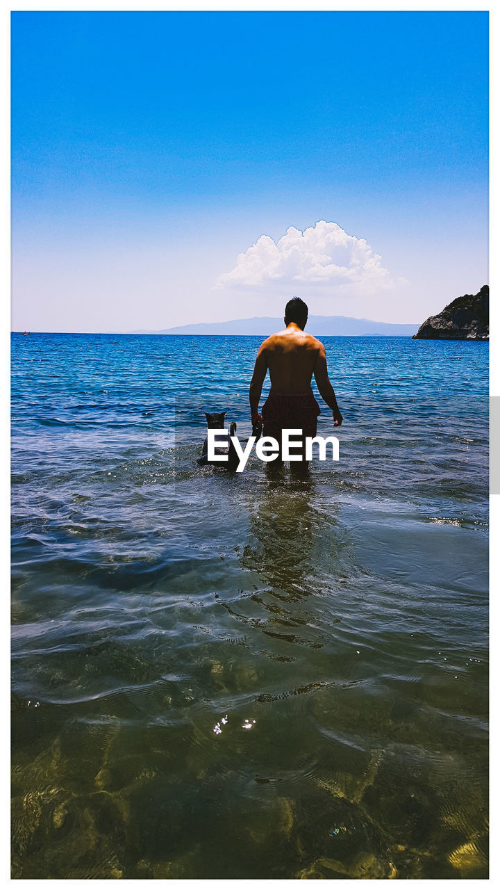 FULL LENGTH REAR VIEW OF MAN ON BEACH AGAINST SKY