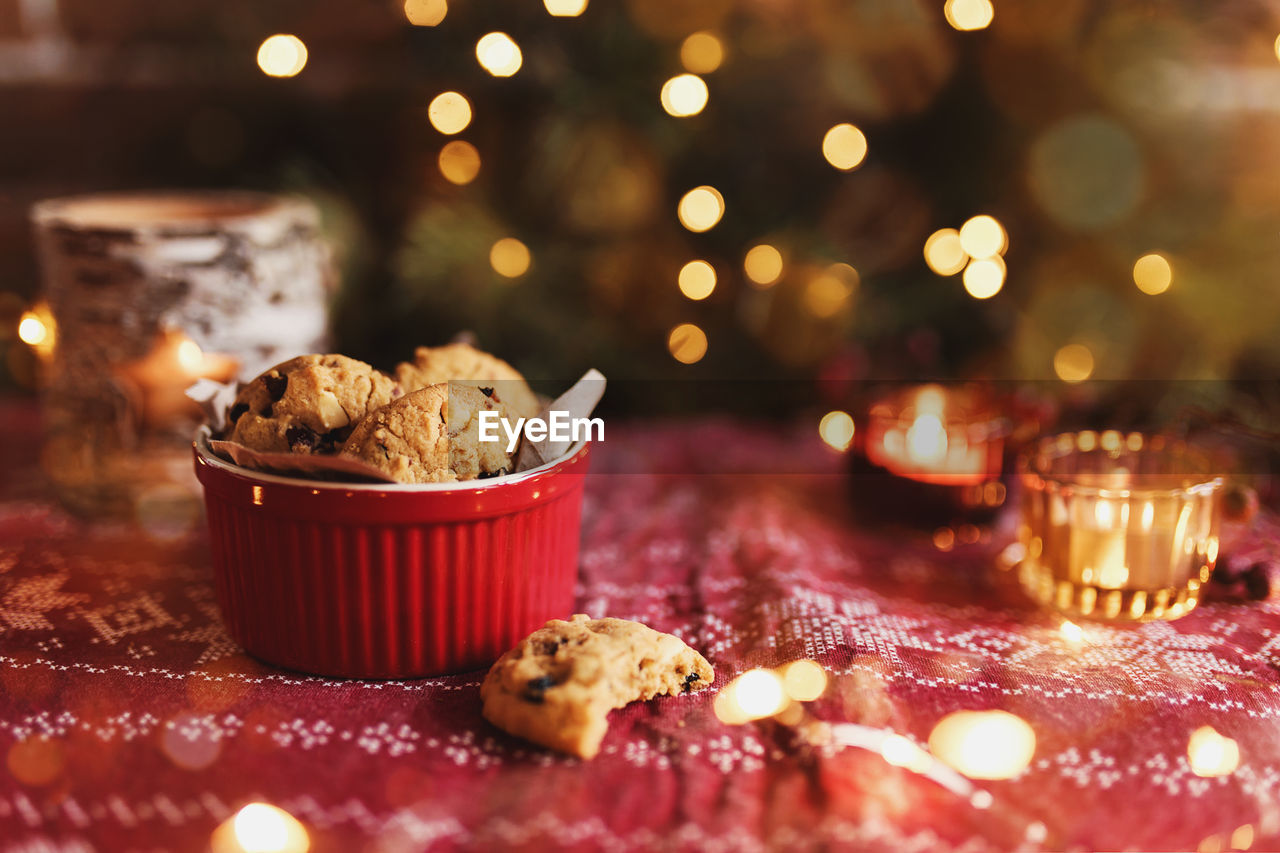 Red festive bowl full with christmas cookies, blurred christmas fir tree lights