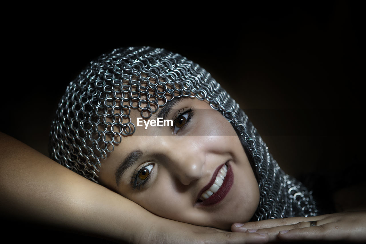 Portrait of smiling teenage girl wearing chain mail over black background