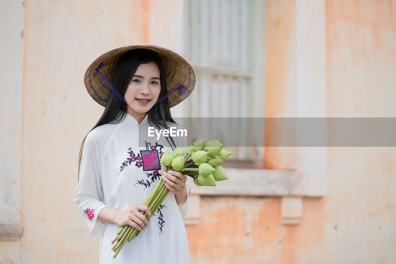Portrait of smiling young woman holding buds against old building