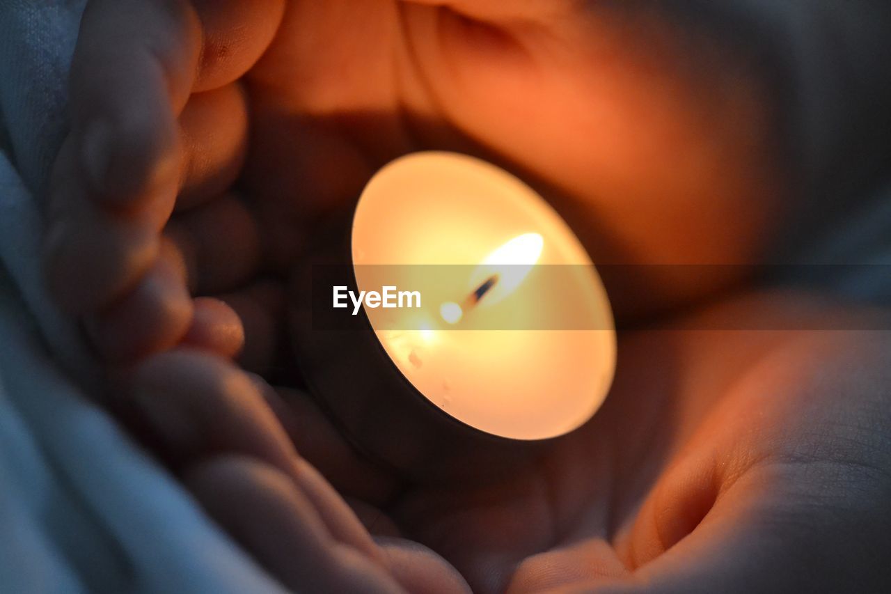 CLOSE-UP OF HUMAN HAND ON ILLUMINATED CANDLE