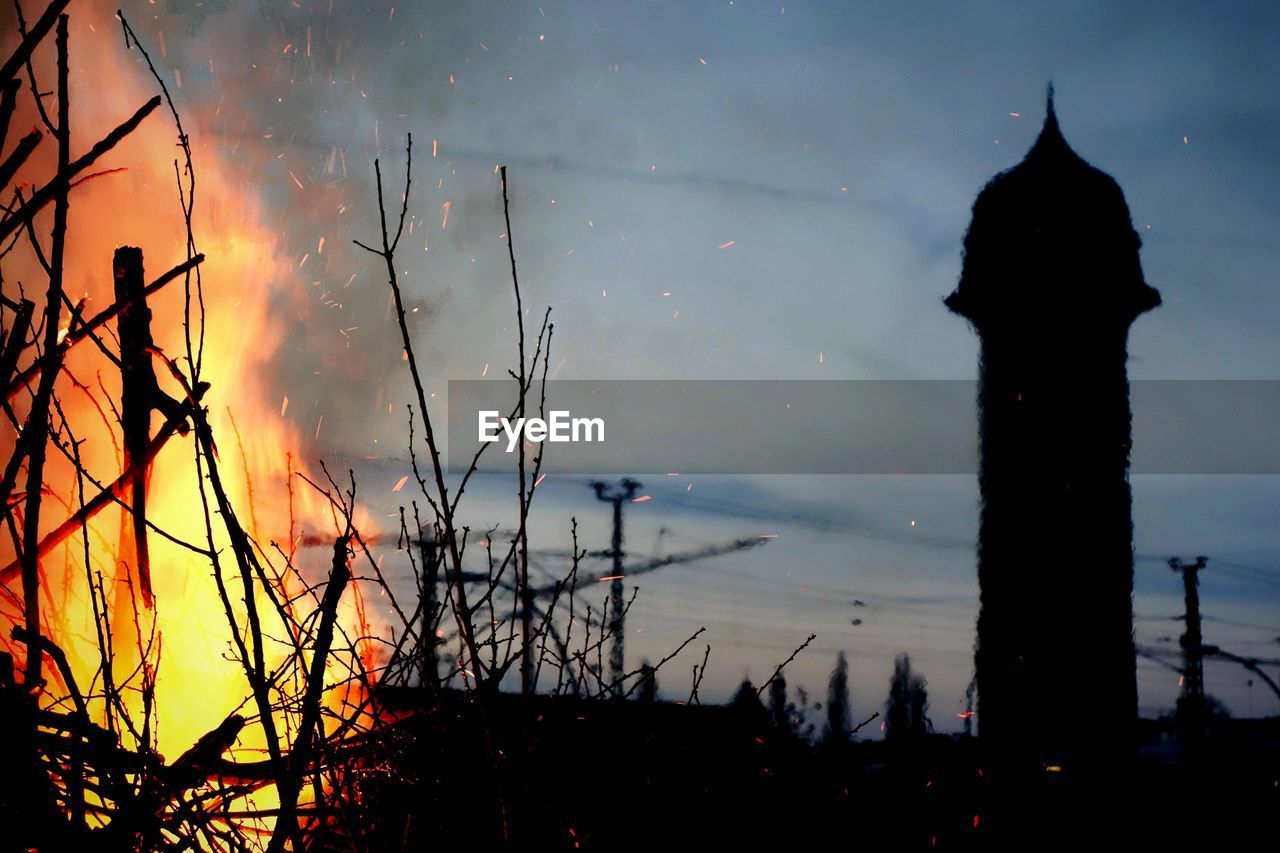 Bonfire against silhouette tower during dusk