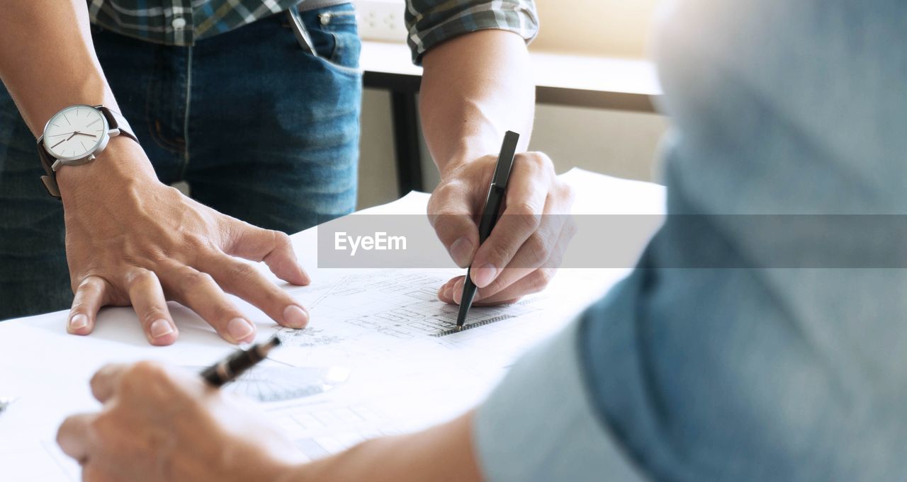 midsection of business colleagues working on blueprint