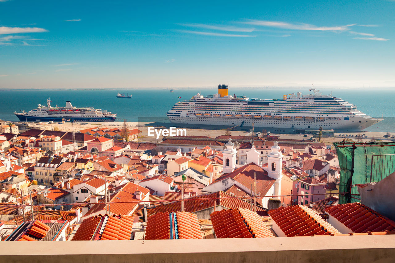 Modern ships moored in lisbon cruise port near houses with red tiled roofs against blue sky on sunny day in portugal