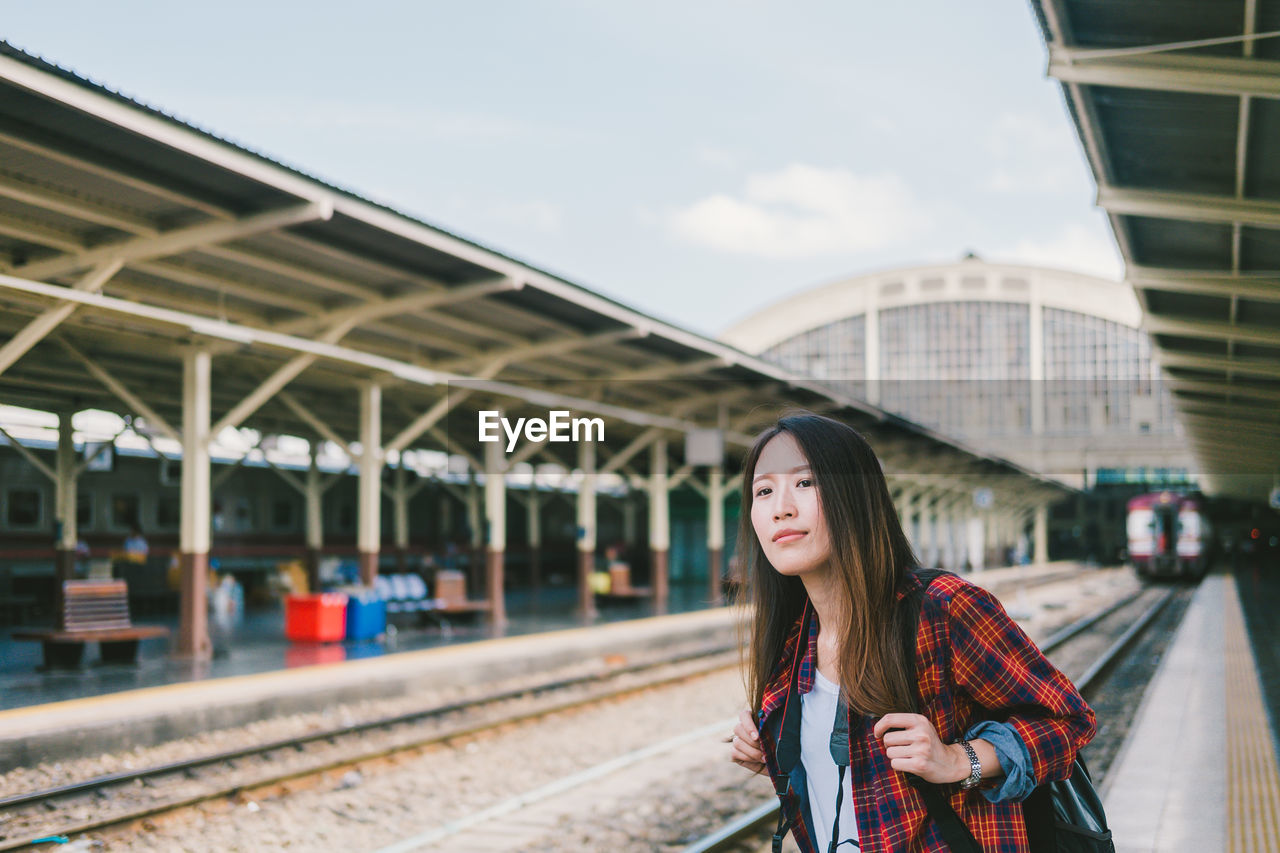 Portrait of smiling young woman standing on railroad station platform