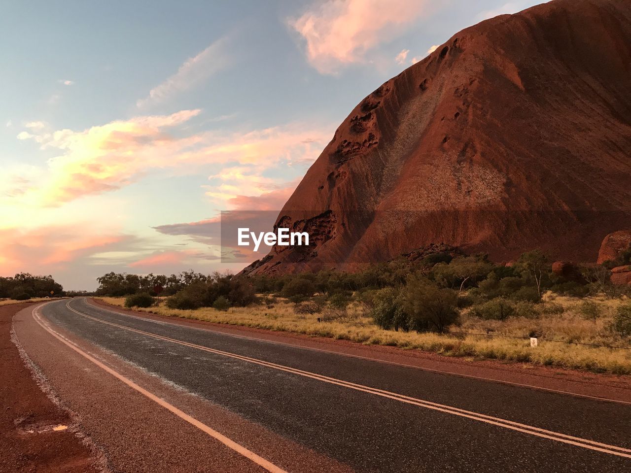 ROAD AMIDST ROCKS AGAINST SKY AT SUNSET