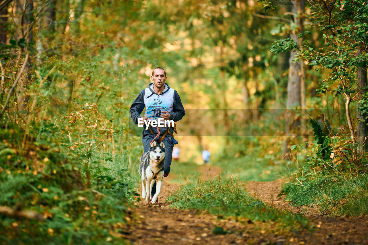 WOMAN WITH DOG RUNNING ON STREET IN FOREST