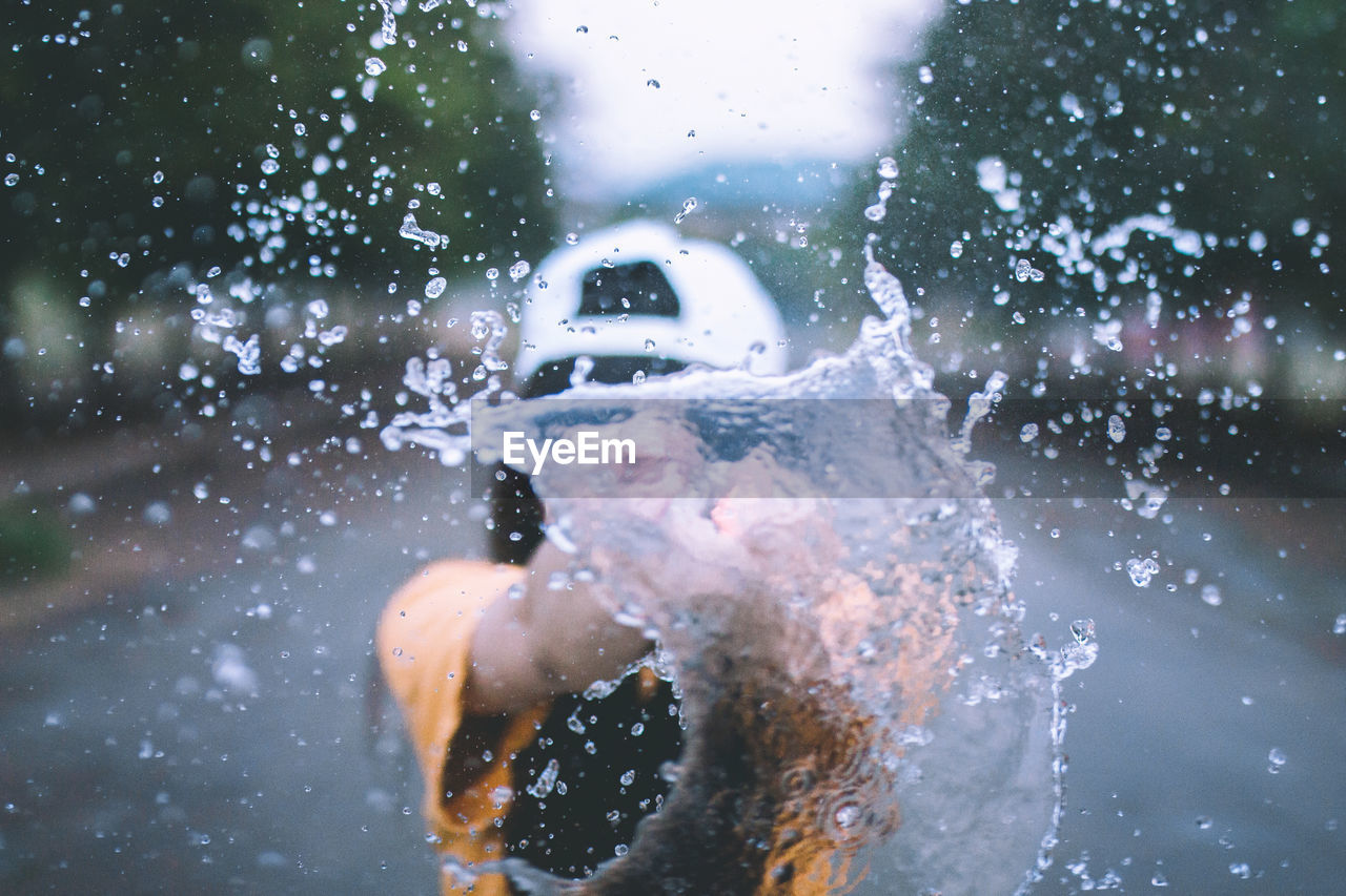 Playful woman splashing water while standing on road