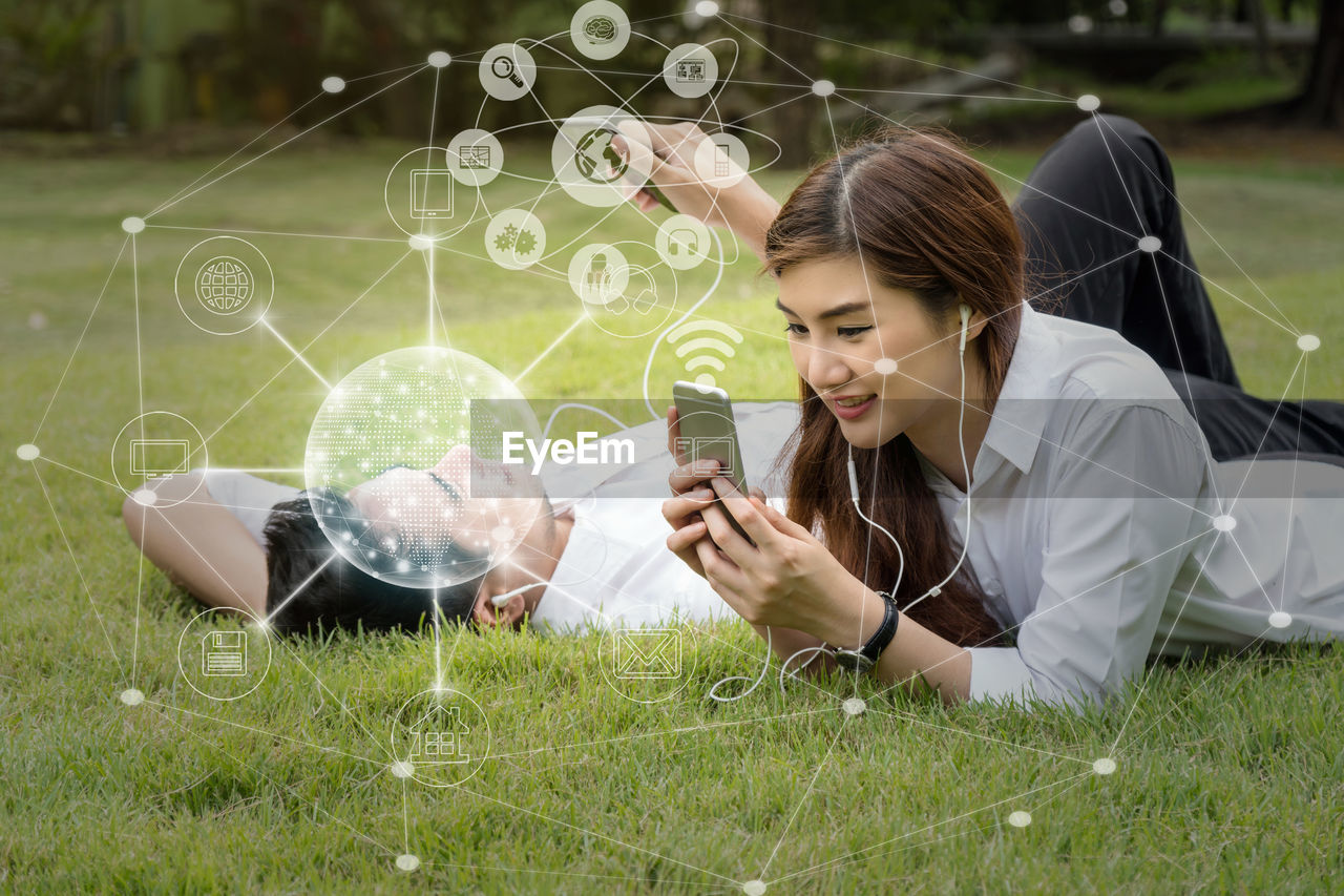grass, plant, adult, nature, women, technology, young adult, lawn, communication, one person, wireless technology, holding, sitting, looking, leisure activity, casual clothing, outdoors, day, smiling, happiness, field, plain, emotion, lifestyles, enjoyment, meadow, internet, relaxation, female, environment, person, brown hair, land, child, computer network