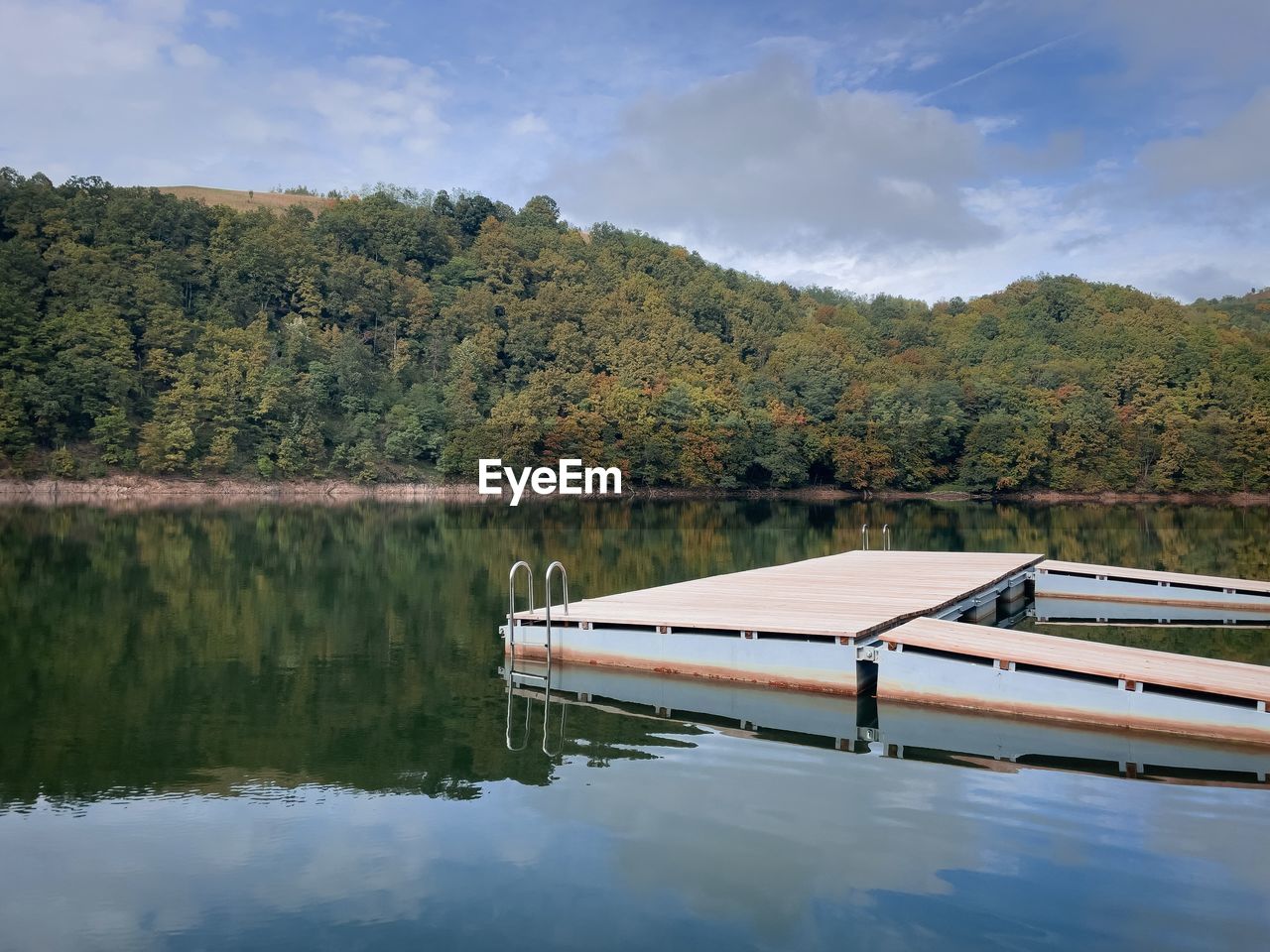 Wooden pontoon on a lake surrounded by forest beginning to change colors in autumn