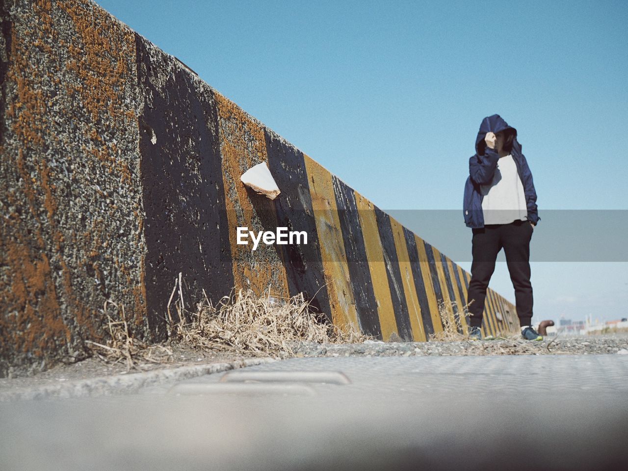 LOW ANGLE VIEW OF YOUNG WOMAN STANDING AGAINST BUILT STRUCTURE