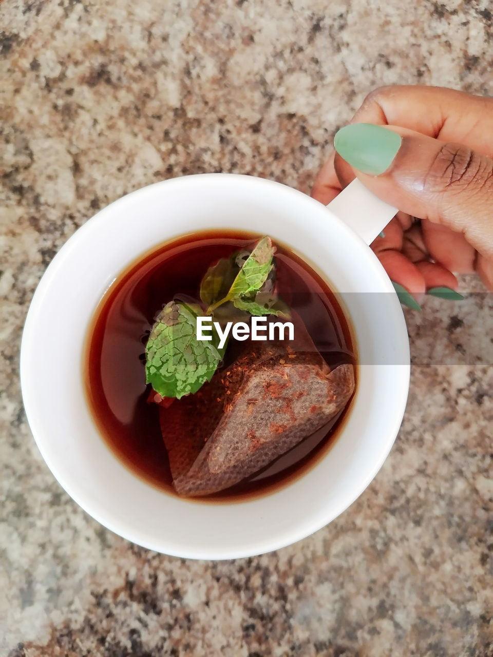 Close-up of hand holding mug with tea and mint leaves