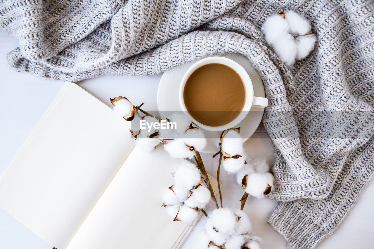 Cup of coffee with cotton plant notebook cinnamon sticks and anise star on white background. sweater 