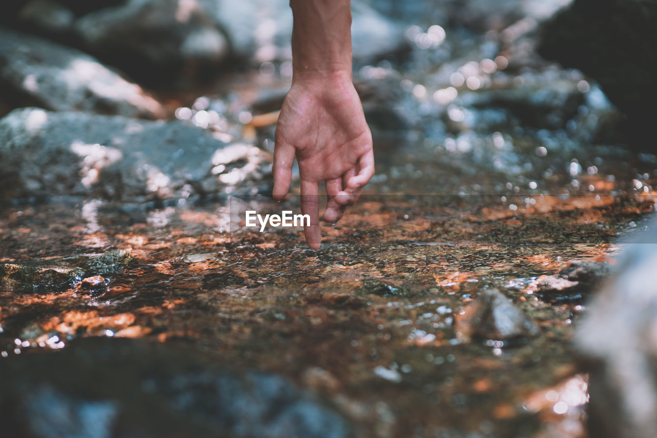Cropped hand touching water flowing in stream