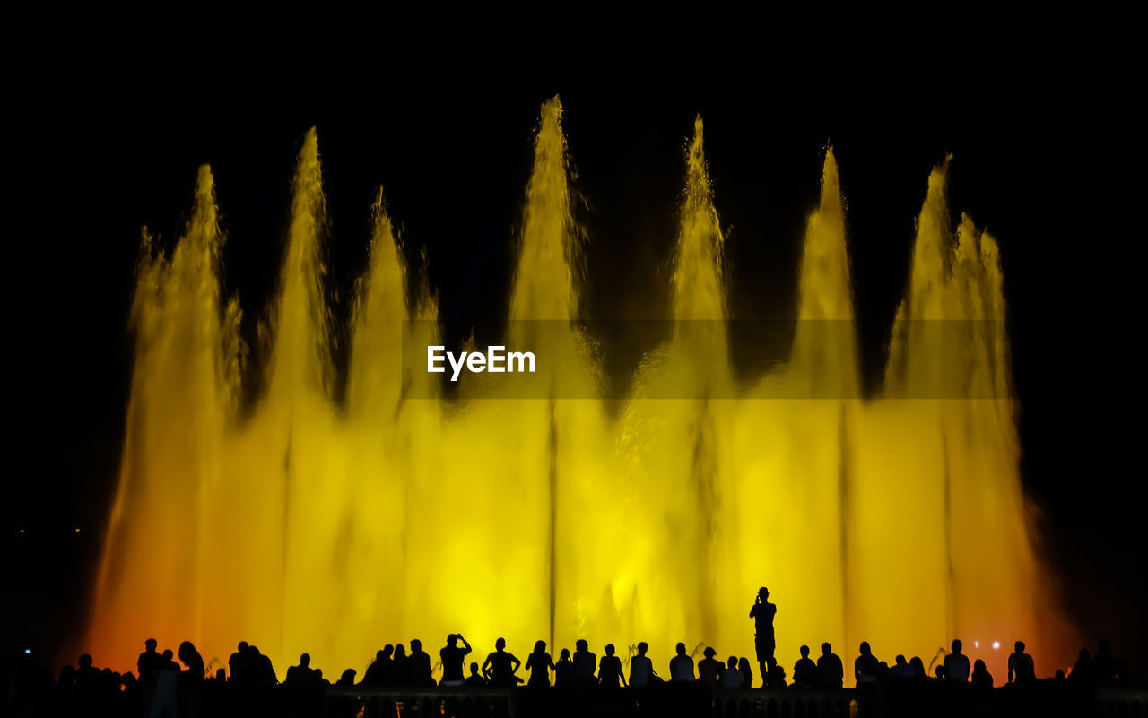 Silhouette of people at night in front of a fountain